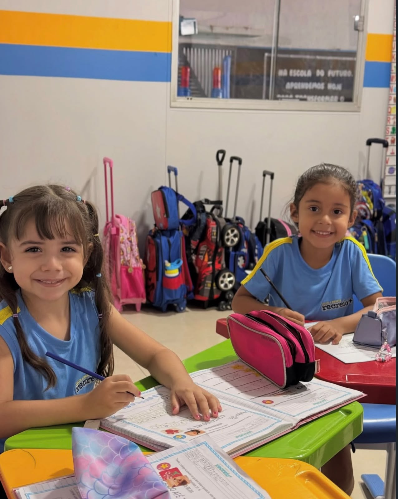 Duas alunas sorrindo enquanto realizam atividade no caderno
