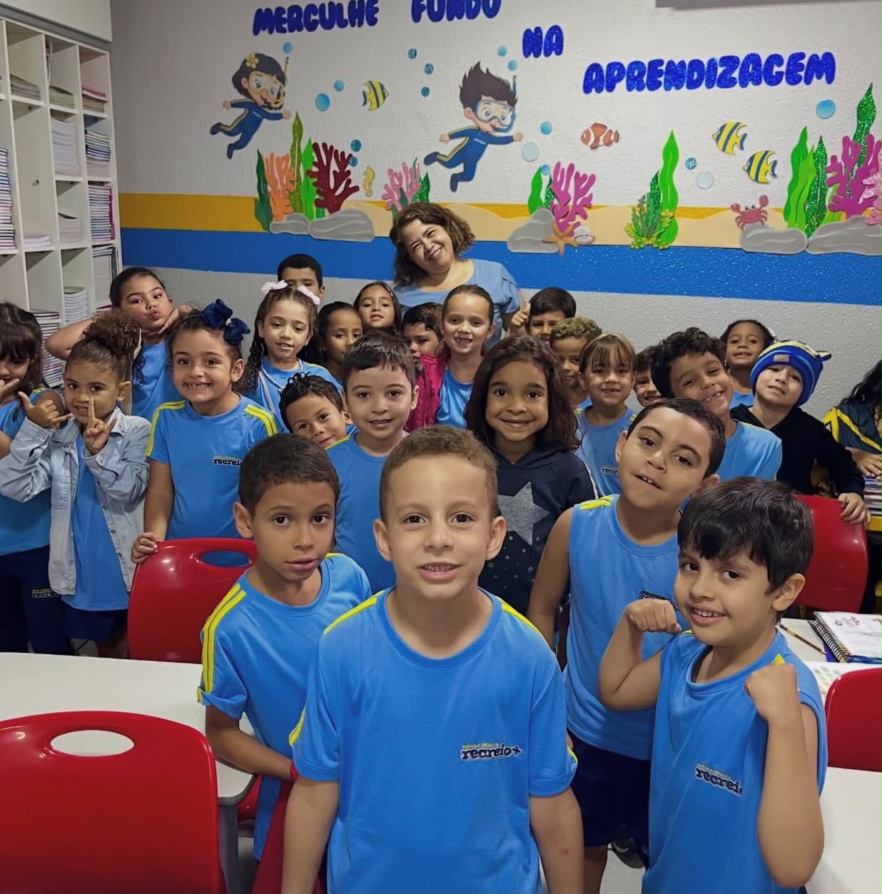 Turma sorrindo em frente ao mural 'Mergulhe fundo na aprendizagem'