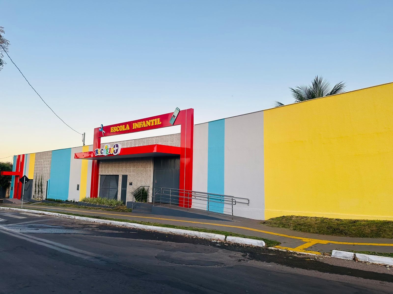Vista lateral da fachada da Escola Infantil Recreio+ com muro amarelo e azul